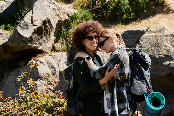 A young lesbian couple hikes through a rocky wilderness area, embracing and enjoying their time together.