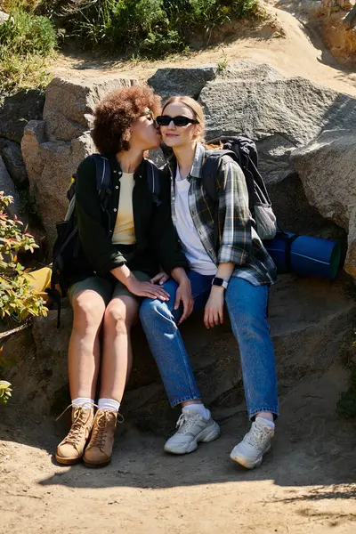 stock image A young lesbian couple enjoys a hike in the wilderness, sharing a tender moment on a rocky outcrop.