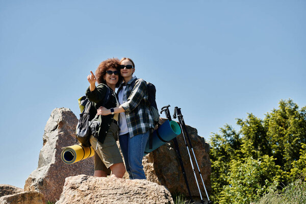 A young lesbian couple hikes in the wilderness, embracing on a mountaintop.