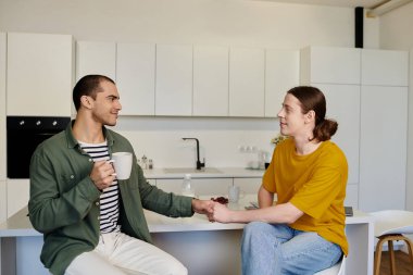 A young gay couple enjoys a morning coffee together in their modern kitchen. clipart