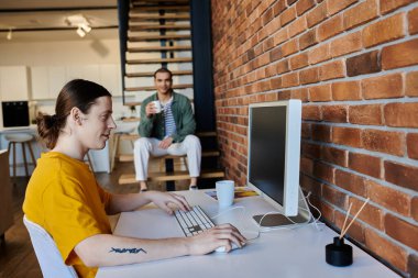 A young gay couple spends a casual afternoon in their modern apartment. One partner works at a desk while the other relaxes nearby. clipart