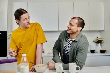 Two young men, dressed casually, enjoy breakfast together in a modern apartment. clipart