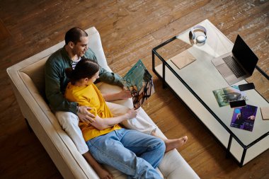 A young gay couple relaxes on a white couch in a modern apartment, enjoying a moment together while looking at a magazine. clipart