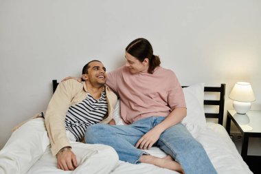 Gündelik giysiler içinde genç bir eşcinsel çift, modern bir dairede bir yatakta birlikte gülüyor ve rahat bir an yaşıyor..
