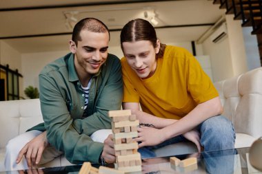 A young gay couple plays a game of blocks in their modern apartment. clipart