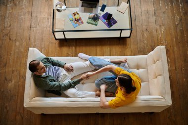 Genç eşcinsel bir çift modern bir dairede beyaz bir kanepede dinleniyor, birlikte sakin bir anın tadını çıkarıyorlar..