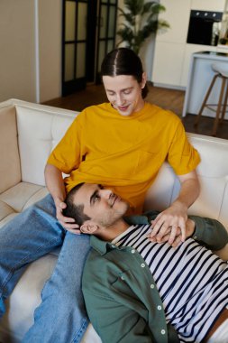 Genç bir eşcinsel çift, modern bir dairede bir kanepede hassas bir yakınlık anlarını paylaşıyor..