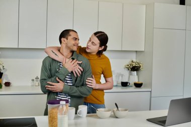 A young gay couple embraces in a modern kitchen, sharing a loving moment as they enjoy their morning together. clipart