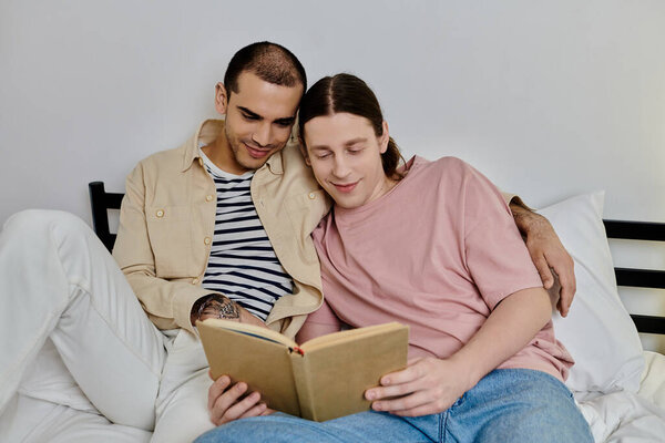 Двое молодых людей, гей-пара, отдыхают на кровати в своей современной квартире и вместе читают книгу.