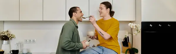 stock image A young gay couple shares a lighthearted moment in their modern apartment, playfully feeding each other breakfast.