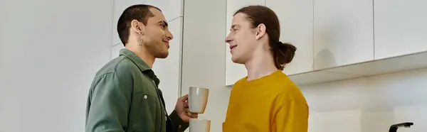 stock image A young gay couple enjoys a casual morning together in their modern kitchen, sharing a warm drink and smiles.