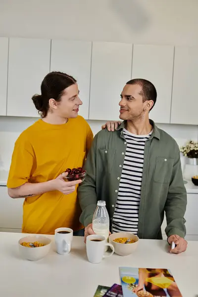 stock image A young gay couple enjoys a casual morning together in their modern apartment, sharing bowl of cherries.