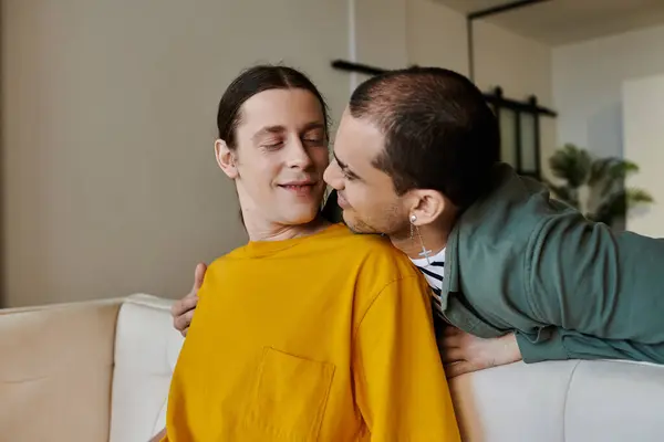 stock image A young gay couple cuddles on a couch in a modern apartment, sharing a loving moment.