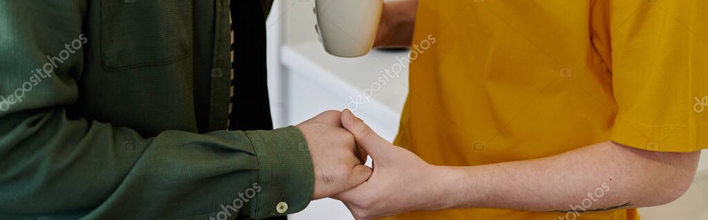 A young gay couple holds hands in their modern apartment, enjoying a quiet moment together.