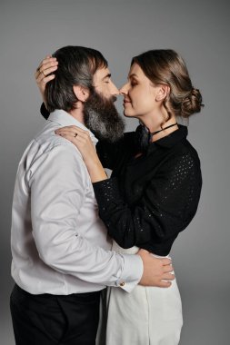 Sofistike giyinmiş sevgi dolu bir çift gri bir arka plana karşı birlikte poz verir..