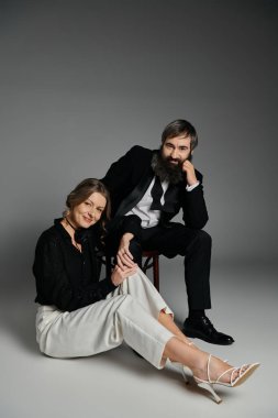 Resmi giyinmiş bir çift, gri bir zemine karşı birlikte poz verir..