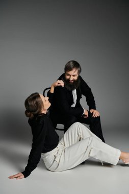 Zarif giyinmiş sevgi dolu bir çift, gri bir zemine karşı birlikte poz verir..