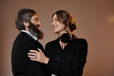 Zarif giyinmiş bir çift hassas bir anı paylaşır, gözleri sevgi dolu bakışlarla kilitlenir..