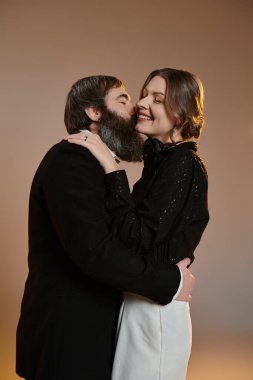 Sofistike giyinmiş bir çift hassas bir anı paylaşıyor, kadın adamı yanağından öpüyor..