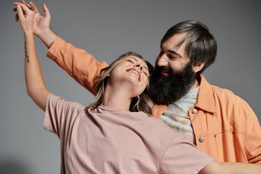 Sevgi dolu bir çift birlikte poz verir, turuncu ceketli adam ve pembe gömlekli kadın, gri arka planda..