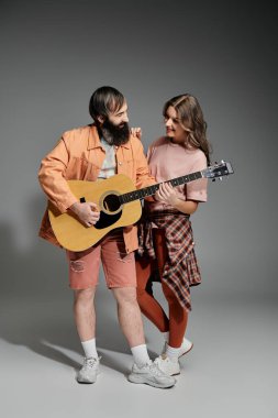 Bir çift stüdyoda birlikte poz verir, adam gitar çalarken kadın eğilir ve gülümser..