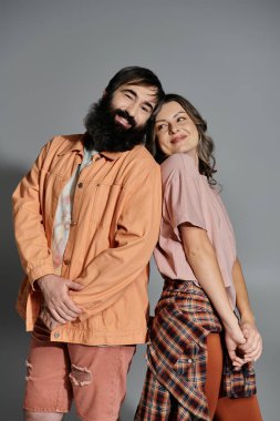 Şık giyinmiş bir kadın ve bir erkek birbirlerine yakın dururlar, sevgi dolu ve samimi bir bağ gösterirler..