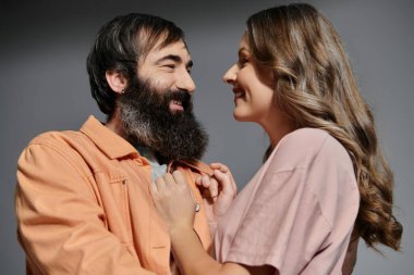 Gri bir arka plana karşı hassas bir anı paylaşan şık giyinmiş bir çift..
