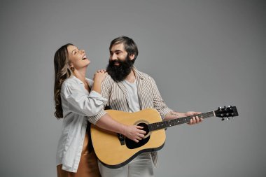 Bir adam eşi için gitar çalar, birlikte bir an eğlenirken gülümser ve güler..
