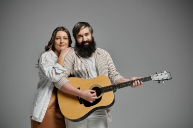 Sofistike giyinmiş bir erkek ve kadın, akustik gitar çalan bir adamla birlikte poz verirler..