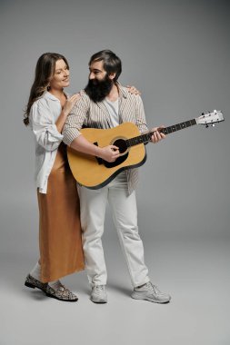 Bir çift stüdyoda birlikte poz veriyor, erkek gitar çalarken kadın sevgiyle izliyor..