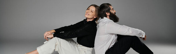 Любящая пара сидит спиной к спине, одетая в сложный наряд на сером фоне.