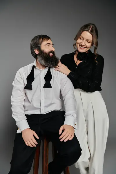 stock image A man and woman in elegant attire pose together against a grey backdrop.