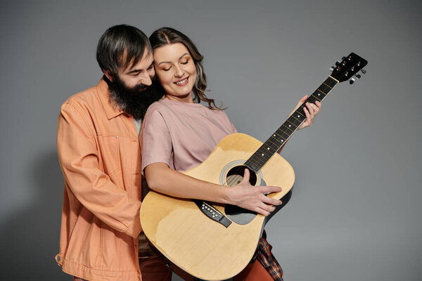 A couple poses together, the woman holding an acoustic guitar.
