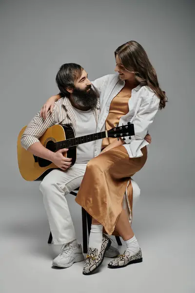 stock image A couple poses together, the man playing a guitar while the woman sits on his lap, their eyes locked in a loving gaze.