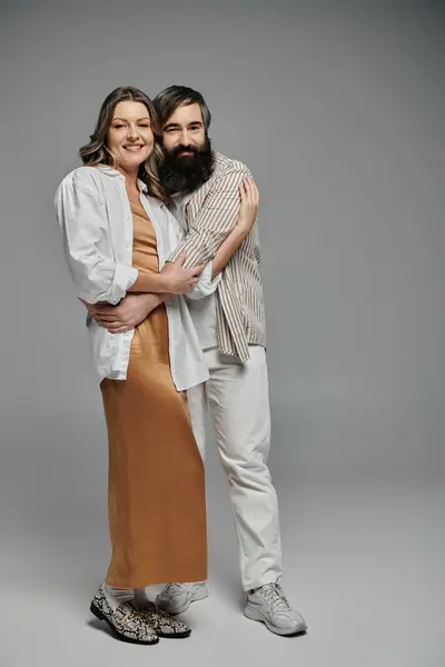 stock image A couple, dressed in elegant outfits, pose together against a simple grey backdrop.