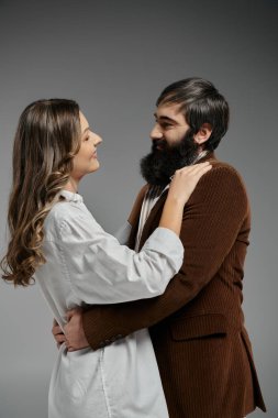 Sofistike giyinmiş, sevgi dolu bir çift, tarafsız gri bir zemine karşı birbirlerini kucaklarlar..