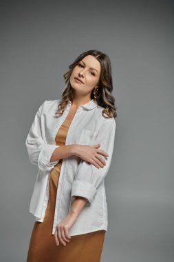 Beyaz gömlekli, kendine güvenen ve zarif bir kadın poz verir..