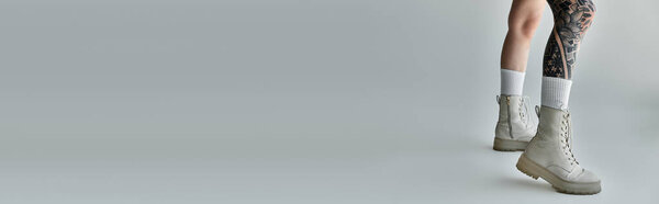 Татуированные женские ноги в боевых сапогах и носках на сером фоне.