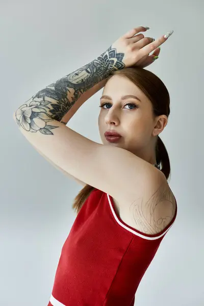 stock image A young woman with tattoos on her arms and shoulders poses in a red tank top and plaid skirt.