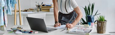 Genç bir adam, eski kıyafetlere yeni bir hayat verecek malzemeler ve araçlarla çevrili DIY giysi restorasyon atölyesinde bir tasarım üzerinde çalışıyor..