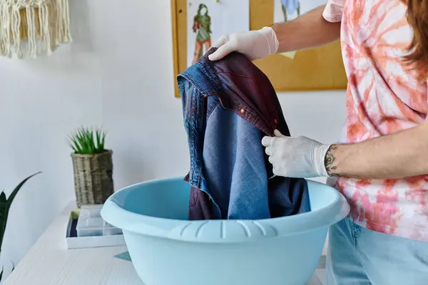 stock image A young man in a DIY clothing restoration atelier dips a denim garment into a basin, transforming discarded clothing into new pieces.