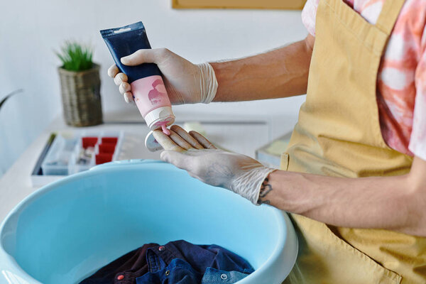 Молодой человек осторожно наносит краску на одежду в своем ателье по реставрации одежды..