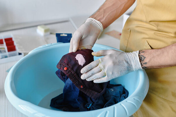 A young man wearing gloves carefully washes a stained piece of clothing in a basin.
