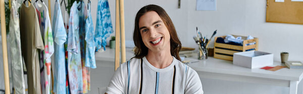 A young man smiles proudly in his DIY clothing restoration atelier, surrounded by racks of upcycled garments.