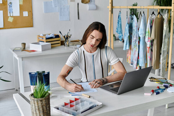 A young man sketches designs at his clothing restoration atelier, surrounded by colorful, upcycled garments.