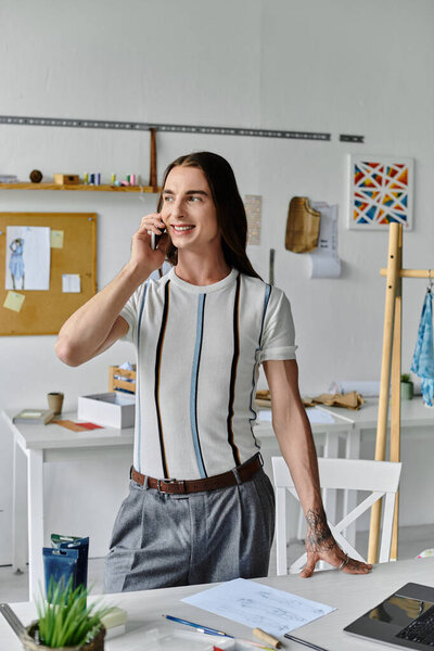 A young man, a DIY clothing restoration atelier owner, speaks on the phone while standing in his workshop.
