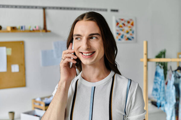 A young gay man, owner of a DIY clothing restoration atelier, smiles while speaking on the phone.
