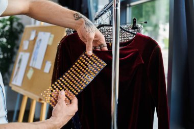 Genç bir adam atölyesindeki kadife bir elbisenin üzerine elmasları dikkatlice yerleştiriyor ve sürdürülebilir giysi restorasyonuna olan bağlılığını gösteriyor..