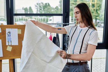 Gey bir adam, DIY giysi restorasyon atölyesi sahibi, yeni bir tasarım üzerinde çalışırken kumaşı inceliyor.
