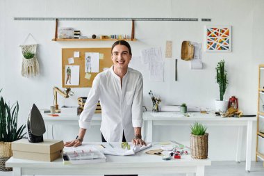 Genç bir tasarımcı, DIY giysi restorasyon atölyesinde dikilirken kendinden emin bir şekilde gülümsüyor. Sürdürülebilir uygulamalarıyla atılmış kıyafetlere yeni bir hayat verme konusunda tutkuludur..